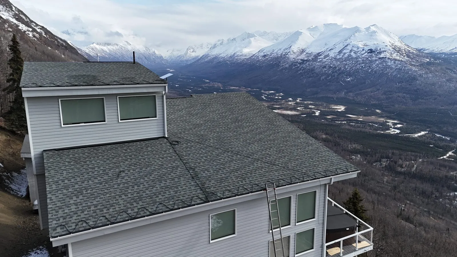 Drone view of a heat cable installation on a hillside Anchorage roof with the Chugach mountains behind