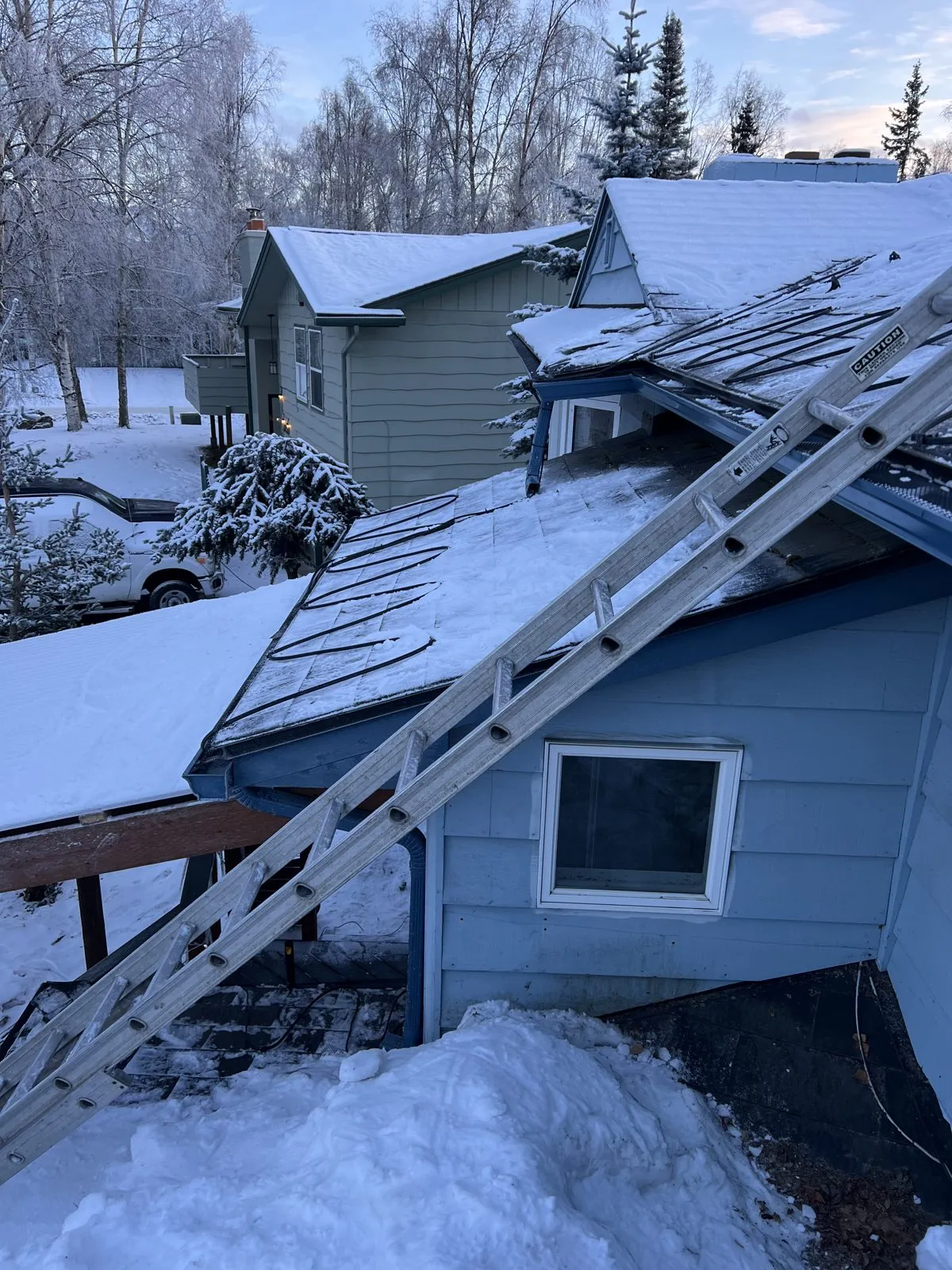 Alaska Heat Cable technician on a ladder during a winter heat cable install